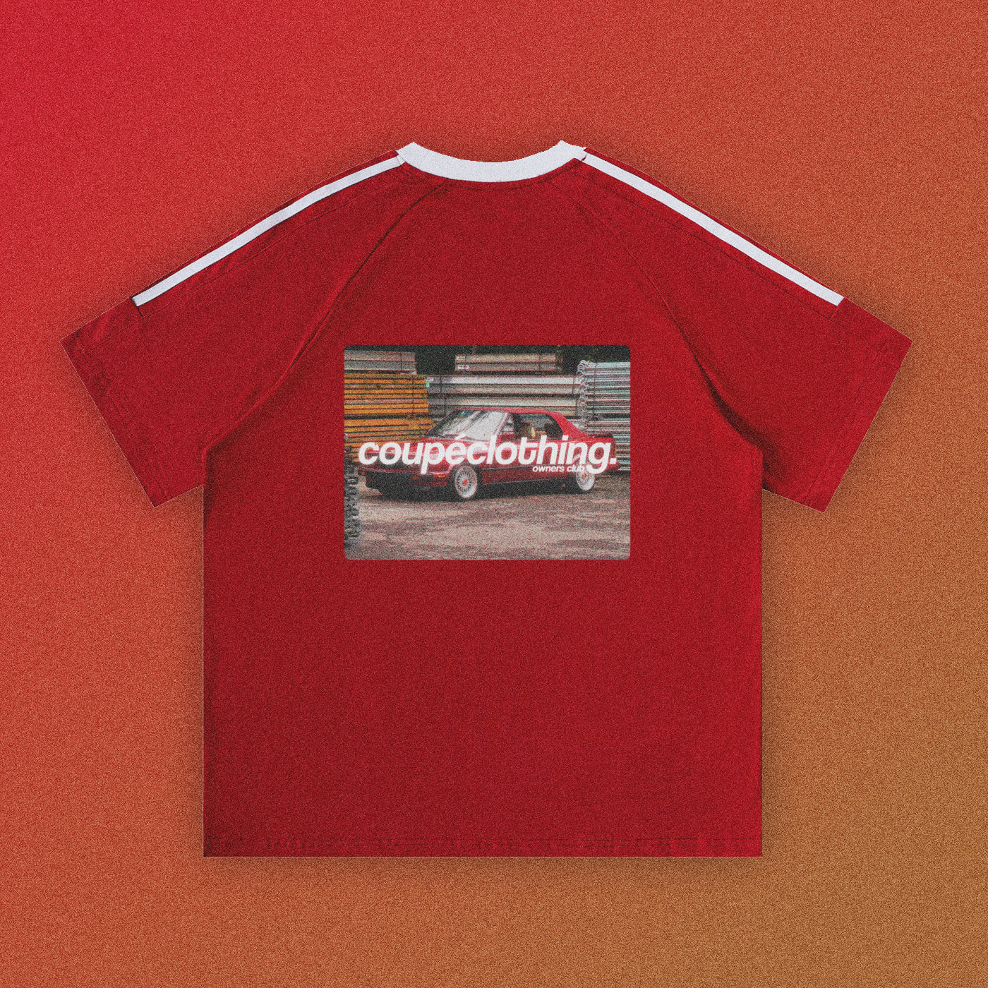 Back of the red 'Owners Club Varsity' t-shirt, which features a contrast white collar and vertical stripe on sleeves. The 'Owners Club' Logo is present in the center, above a design featuring an image of a car.